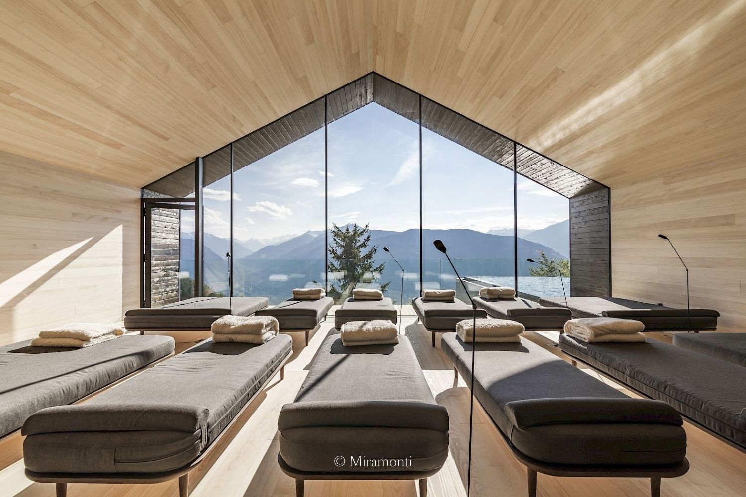 A cabin like hotel communal space, with chaise lounge chairs, side lamps, overlooking the mountains.