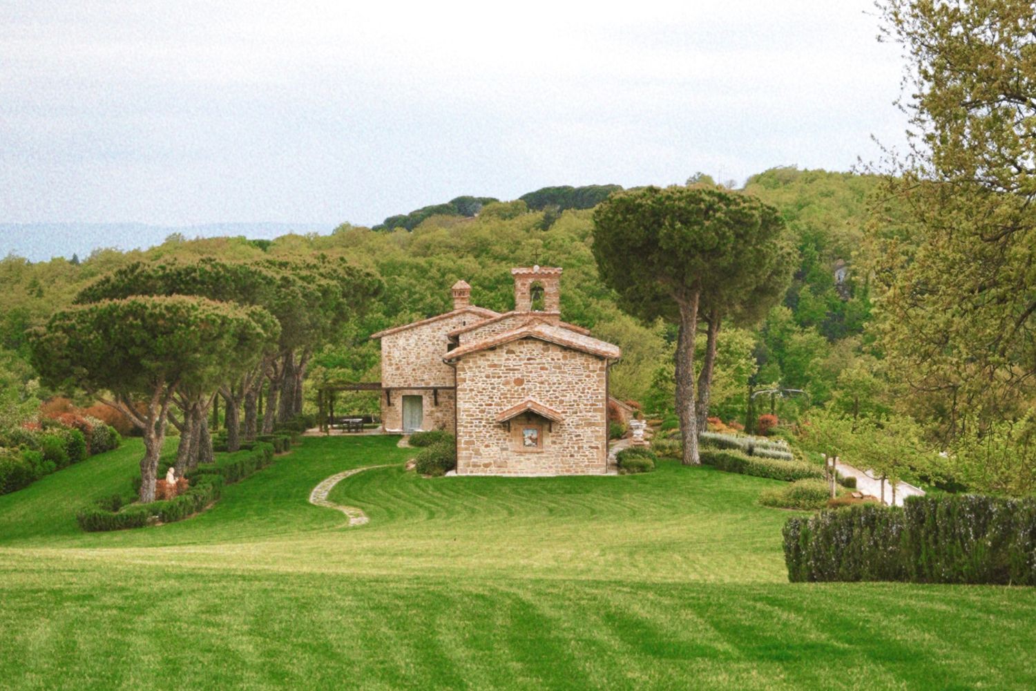 A cobbled stone house, surrounded by a green scenery of trees, bushes and grass.