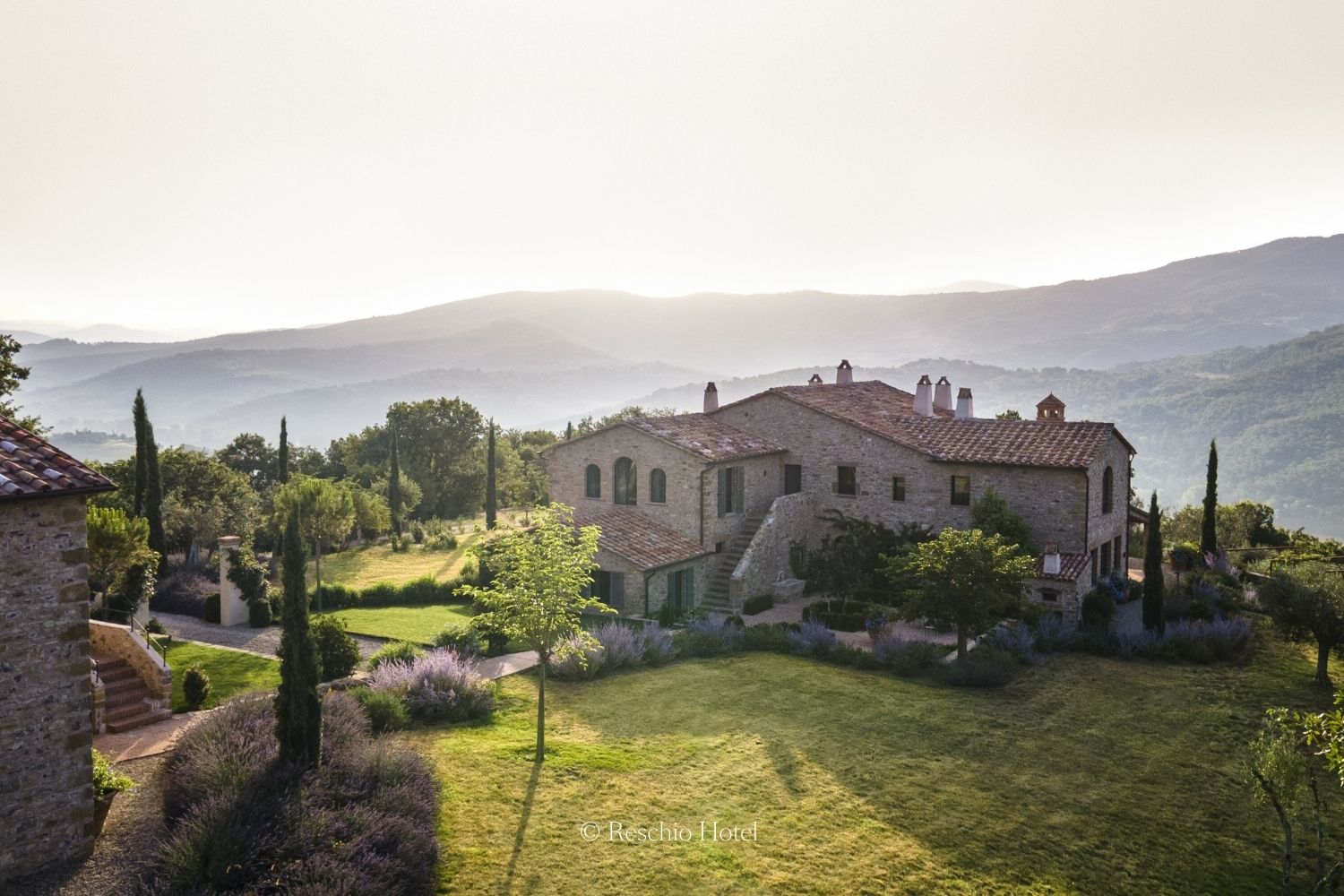 Cobbled stone houses on top of a hill, surrounded by mountains, trees, bushes and grass.