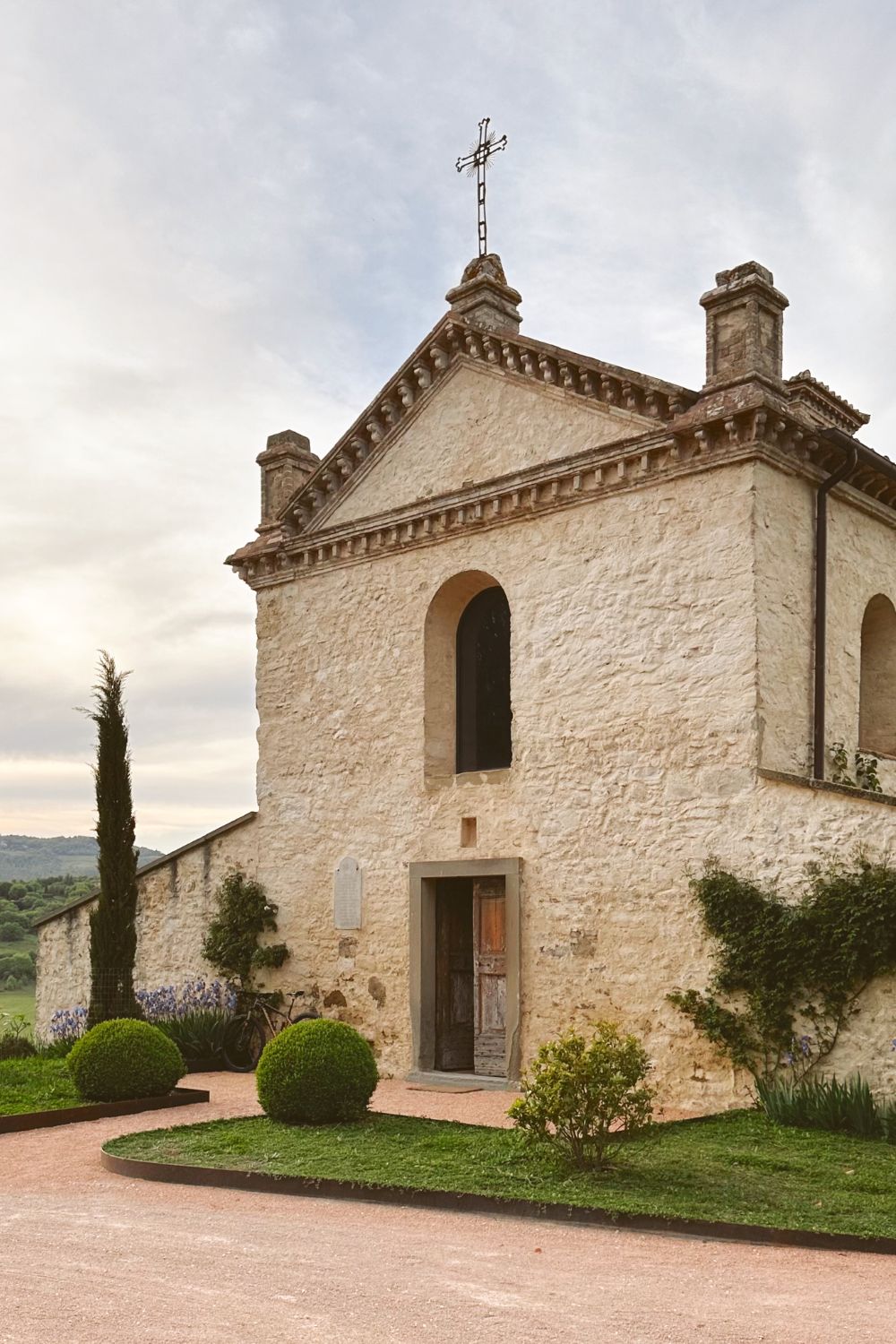 Cobbled stone church on top of a hill, surrounded by mountains, trees, bushes and grass.