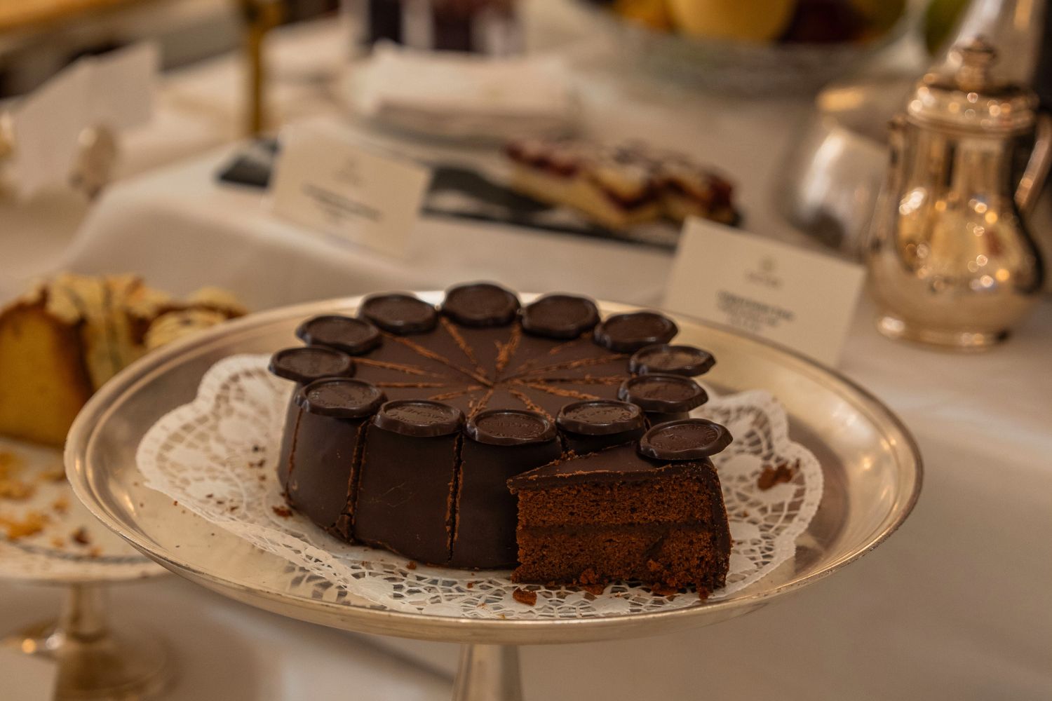A dark chocolate cake on a silver stand, next to other sweets.