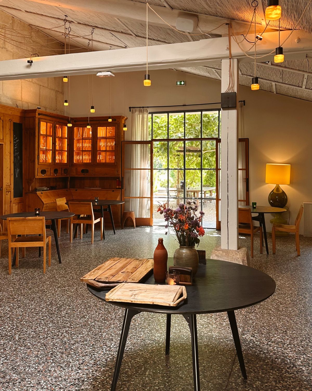 Indoor restaurant space with wooden and black iron furniture, white beams on the ceiling and hanging lights.