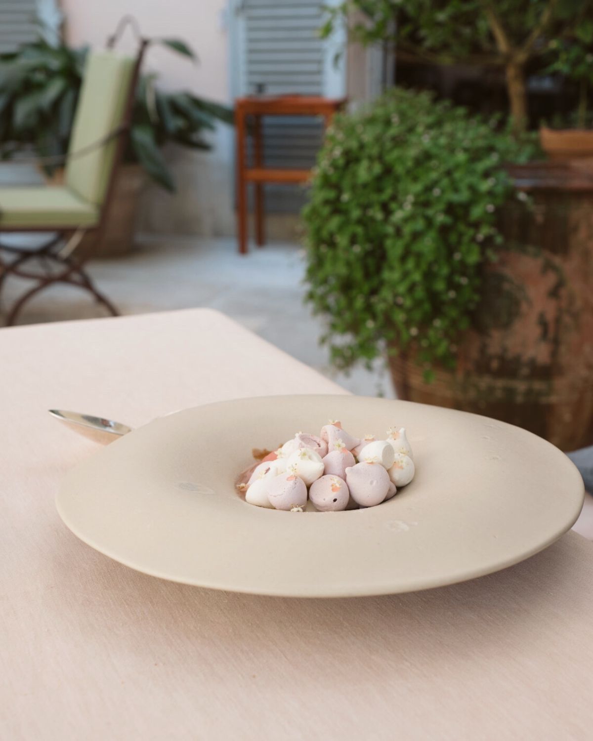 Grey oval plate with small pastel colored pastries, on top of a linen tablecloth on an outdoor setting.