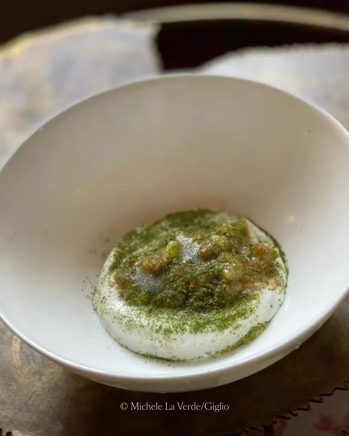 Green powder over a white rounded paste, inside an oval deep bowl, on a dark brown surface.