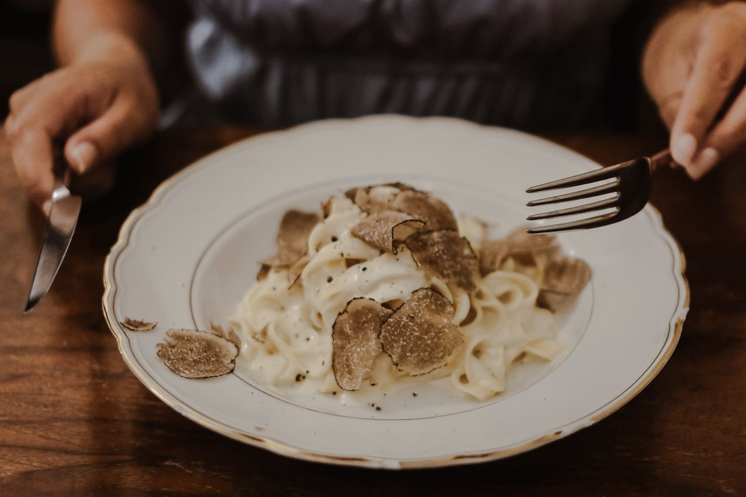 Classic white dish with pasta in cheese and oysters. A Lady's hands holding a fork and a knife over a wooden table.